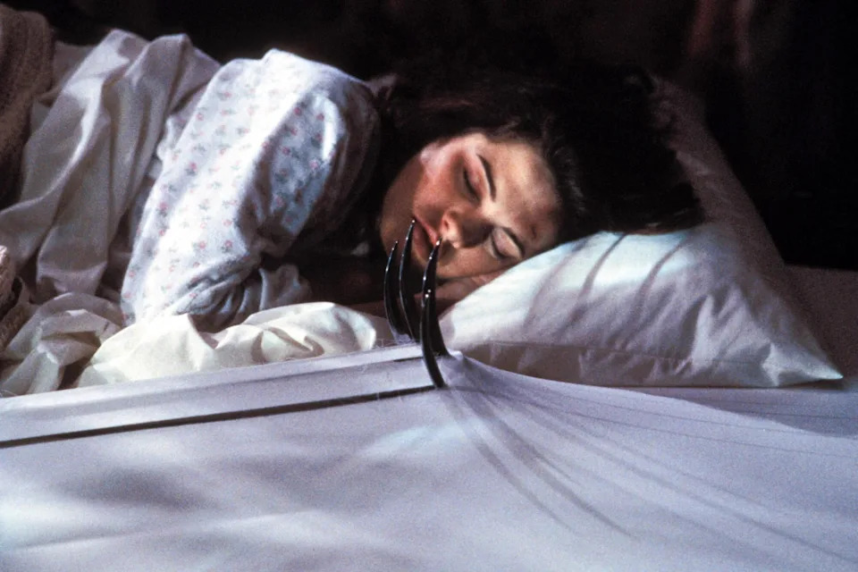 Nancy sleeps as Freddy Krueger's bladed glove reaches across the bed in A Nightmare on Elm Street